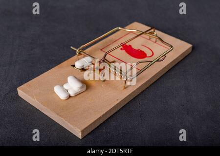 Compresse mediche poste in un mousetrap. Una trappola per le persone sotto forma di prodotti farmaceutici. Sfondo scuro. Foto Stock