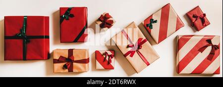 Piatto-lay di scatole regalo artigianato festivo in carta da imballaggio decorata con nastri e archi verdi e rossi su fondo bianco semplice, vista dall'alto. Concetto del giorno di boxe di Natale Foto Stock