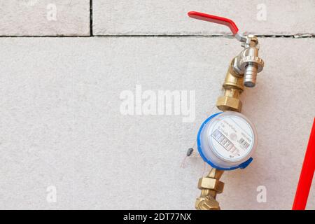 Contatore di acqua fredda con un rubinetto all'ingresso dell'acqua all'interno della casa sullo sfondo di blocchi di cemento. Dispositivo di misurazione Foto Stock