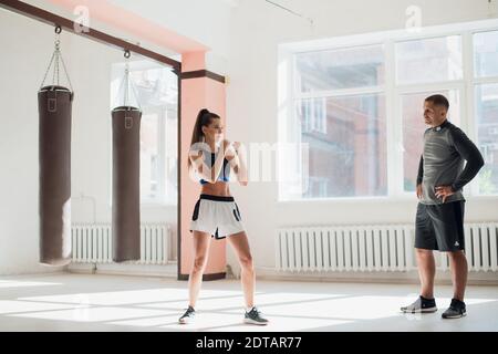 Un giovane pugile attraente insegna le sue tecniche di pugilato ragazza in un loft attrezzato per l'allenamento di pugilato Foto Stock