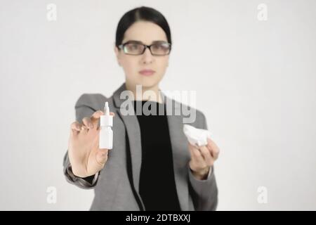 Giovane bella donna in occhiali e giacca grigia che tiene il naso spray di fronte a lei. Messa a fuoco selettiva. Foto Stock