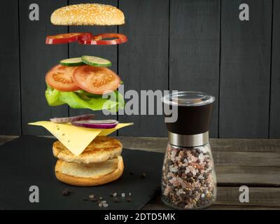 Hamburger volanti. Hamburger o cheeseburger ingredienti volanti su un tagliere di pietra. Burger nell'aria. Posiziona per il testo Foto Stock