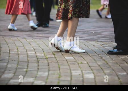 Giovani donne che indossano abiti a pois vintage che ballano nel parco cittadino, vista ravvicinata delle stesse scarpe da ballo nere e calzini bianchi, swing jazz retrò femminile Foto Stock