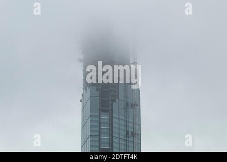 Costruzione di un grattacielo sotto la pioggia. Grattacieli e nuvole con nebbia. Vista dal basso del grattacielo senza finitura Foto Stock