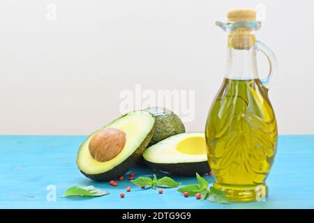 Concetto di cibo sano con avocado tagliato e una bottiglia di olio d'oliva su sfondo blu e bianco. Foto Stock