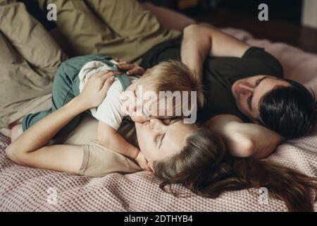 Famiglia felice con il figlio piccolo che giace e gioca a letto a casa Foto Stock