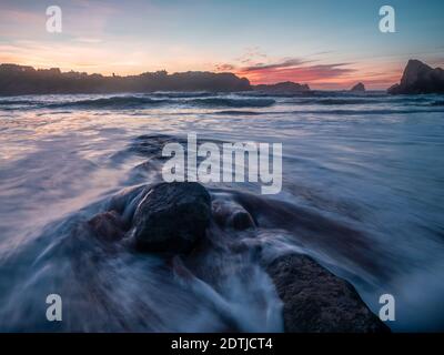 Bellissimo paesaggio della spiaggia di Portio al tramonto a Liencres, Cantabria. Onde che si schiantano contro le rocce. Foto Stock