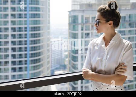 Giovane donna d'affari in piedi accanto alla grande finestra. Ufficio in un edificio moderno della grande città Foto Stock