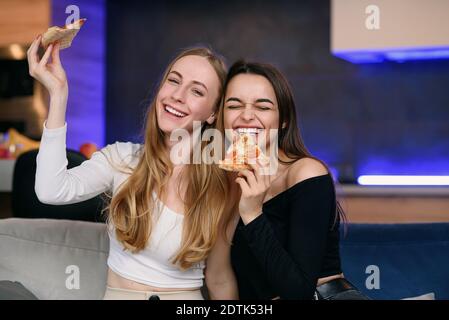 Due migliori amici femminili che si divertono a casa, con gustosa pizza a casa festa. Rimanere a casa e utilizzare la consegna di cibo durante la quarantena. Foto Stock