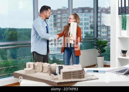 Piacevole esperienza moderna elegante e soddisfatto giovani designer discutere momenti di lavoro utilizzo di un progetto con progetto di nuovi edifici vicino a panoramic win Foto Stock