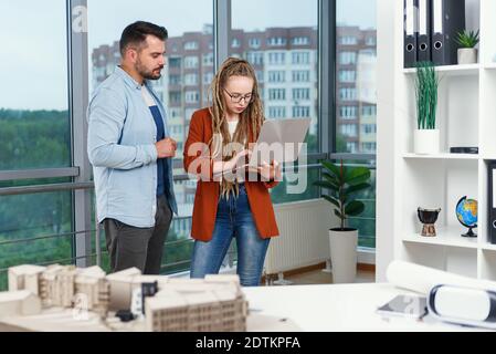Piacevole esperienza moderna elegante e soddisfatto giovani designer discutere momenti di lavoro utilizzo di un progetto con progetto di nuovi edifici vicino a panoramic win Foto Stock