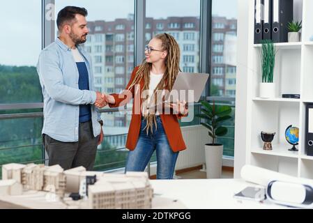 Piacevole esperienza moderna elegante e soddisfatto giovani designer discutere momenti di lavoro utilizzo di un progetto con progetto di nuovi edifici vicino a panoramic win Foto Stock
