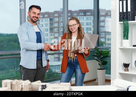 Piacevole esperienza moderna elegante e soddisfatto giovani designer discutere momenti di lavoro utilizzo di un progetto con progetto di nuovi edifici vicino a panoramic win Foto Stock