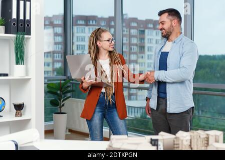 Piacevole esperienza moderna elegante e soddisfatto giovani designer discutere momenti di lavoro utilizzo di un progetto con progetto di nuovi edifici vicino a panoramic win Foto Stock