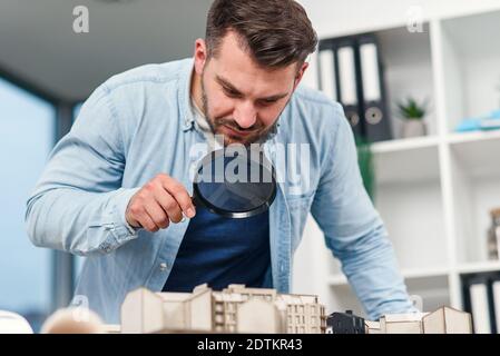 Architetto ispettore esamina un modello di casa utilizzando una lente di ingrandimento. Ispezione della casa e concetto di bene immobile. Foto Stock