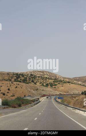 Un'immagine verticale di una strada curvilinea che attraversa un paesaggio asciutto sotto un cielo limpido Foto Stock