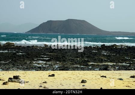 Spagna, Isole Canarie, Fuerteventura, costa rocciosa con l'isola di Los Lobos alle spalle Foto Stock