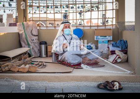 Pescatore arabo, riparando la rete di pesca fatta in casa e yacht di legno, indossando la maschera facciale e si siede sul pavimento del tradizionale boam Foto Stock