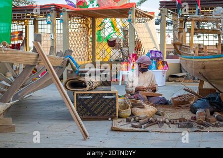 Pescatore arabo, riparando la rete di pesca fatta in casa e yacht di legno, indossando la maschera facciale e si siede sul pavimento del tradizionale boam Foto Stock