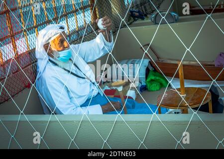 Pescatore arabo, riparando la rete di pesca fatta in casa e yacht di legno, indossando la maschera facciale e si siede sul pavimento del tradizionale boam Foto Stock