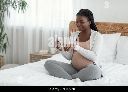 Donna incinta nera che fa lo shopping in linea con lo smartphone a casa Foto Stock