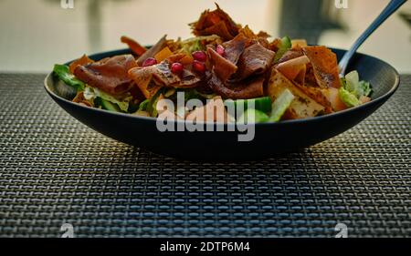 Fatoush (insalata libanese) immagine ravvicinata in un piatto nero . E' fatto con verdure e pane piatto tostato croccante, che insafire il condimento Foto Stock