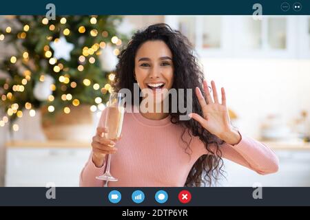 Cheerful Lady con Champagne che sventola la mano alla fotocamera mentre si fa Videochiamata Foto Stock