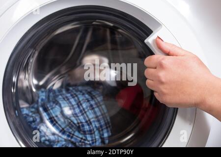 Donna apre la porta della lavatrice in lavanderia. Foto Stock