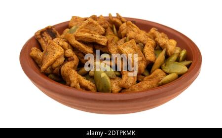 Vista laterale di una piccola ciotola piena di semi di zucca tostati organici con pezzi di mela disidratati isolati su sfondo bianco. Foto Stock