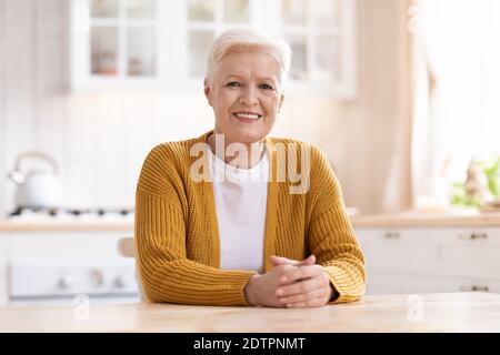 Ritratto di allegra vecchia donna seduta in cucina Foto Stock