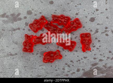 Vista dall'alto di una porzione di colorati gummi rossi portano caramelle di zucchero su uno sfondo grigio chiazzato. Foto Stock