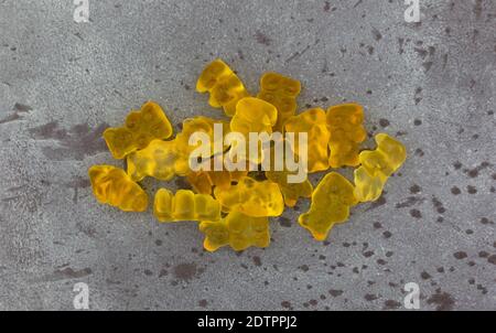 Vista dall'alto di una porzione di colorati gummi gialli portano caramelle di zucchero su uno sfondo grigio chiazzato. Foto Stock