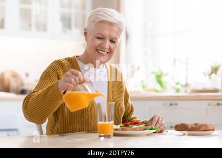 Bella nonna che versa succo, pranzo in cucina Foto Stock