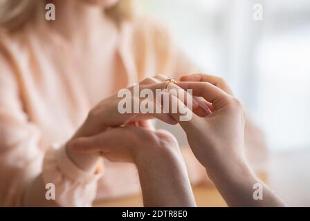 Closeup di giovane uomo che mette anello di fidanzamento del diamante sul dito della sua ragazza, facendo la proposta di matrimonio al caffè Foto Stock
