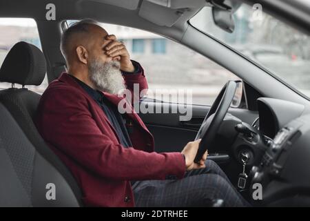 Exhausetd uomo dai capelli grigi invecchiato che ha mal di testa durante la guida dell'auto Foto Stock