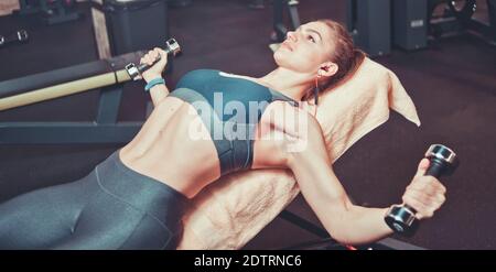 Fitness ragazza in allenamento sportivo con manubri su una panca inclinata in palestra. Allenamento del muscolo toracico Foto Stock
