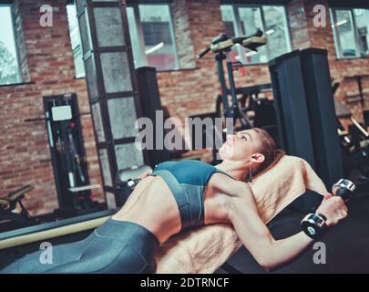 Ragazza sportiva concentrata in allenamento sportivo con manubri su panca inclinata in palestra. Allenamento del muscolo toracico Foto Stock