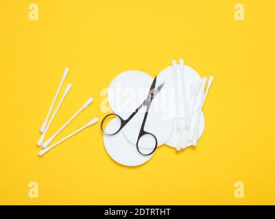 Prodotti igienici per manicure a stay piatto su fondo giallo. Spugnette di cotone, bastoncini di cotone, forbici per unghie. Vista dall'alto Foto Stock