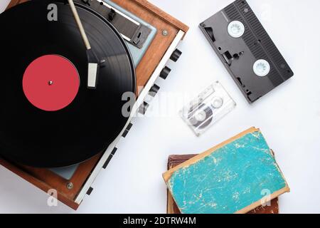 Oggetti retrò cultura pop su sfondo bianco. Lettore di dischi in vinile, libri antichi, audio, videocassette. Vista dall'alto, supporti, disposizione piatta Foto Stock