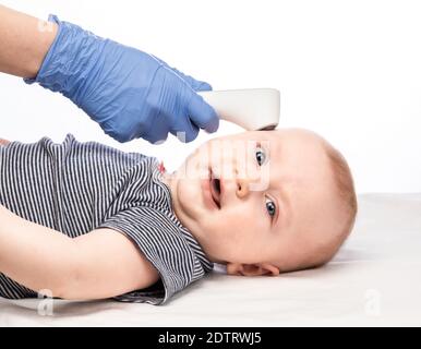 Il pediatra o l'infermiere controlla la temperatura corporea del bambino utilizzando gli infrarossi termometro frontale (termometro a pistola) per i sintomi del virus Foto Stock