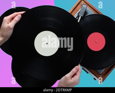 Le mani della donna tengono il disco del vinile, il giocatore del vinile con i dischi su uno sfondo di due colori. Stile retrò, anni '80, vista dall'alto Foto Stock