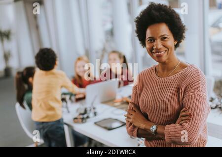 Smily African American insegnante di scienza femminile con gruppo di bambini programmazione di giocattoli e robot elettrici in classe robotica Foto Stock