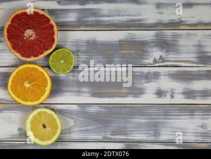 Vista dall'alto su quattro metà di frutta tagliate isolate, pompelmo rosso maturo, limone, lime e arancio su tavola di legno naturale bianco con spazio per la copia del testo Foto Stock