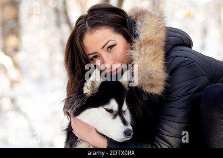 Bella giovane donna abbracciando femmina Husky cane in inverno freddo giornata innevata Foto Stock