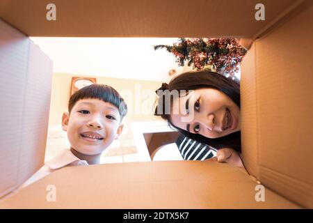 Il bambino sorpreso e mamma disimballaggio, aprendo la scatola di cartone e guardando all'interno. Unboxing vista interna, famiglia asiatica. Foto Stock