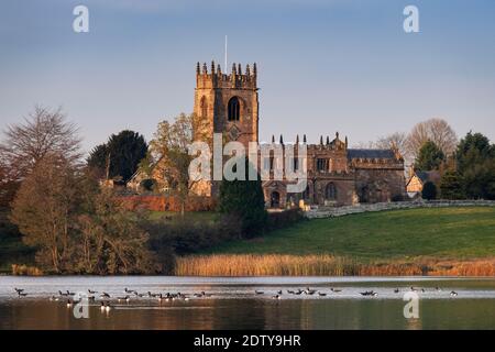 Canada Geese on Big Mere sostenuto dalla Chiesa di San Michele, Marbury, Cheshire, Inghilterra, Regno Unito Foto Stock