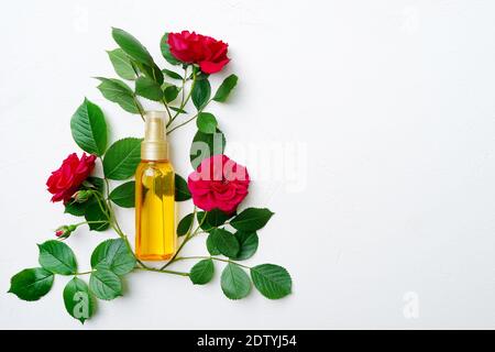 Flacone di vetro giallo con olio cosmetico naturale per la pelle o. capelli con rose rosse su sfondo bianco con una copia spazio Foto Stock