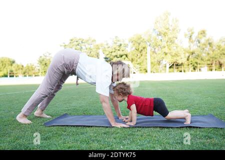 Adulto bella donna e bambina stanno facendo esercizi di yoga al parco con bella natura fuori. Foto Stock