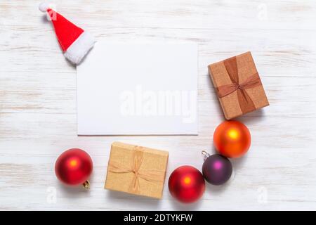 Biglietto d'auguri vuoto con cappello Babbo Natale, palle e confezioni regalo. Mockup vacanza. Concetto di Natale. Disposizione piatta, vista dall'alto, spazio per la copia Foto Stock