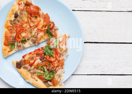 Vista dall'alto di due fette di pizza appena sfornate con formaggio, pomodoro, olive ed erbe su un piatto blu su uno sfondo di legno bianco Foto Stock